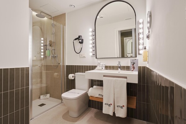 A modern bathroom with a glass-enclosed shower, a white toilet, a vanity with a mirror and lights, and two towels hanging on a rack. - Intelier Villa Katalina Hotel by Intelier Hotels & Suites (San Sebastián)