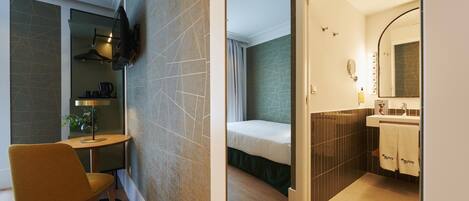 Habitación pequeña con cama, una mesita con silla, televisor montado en la pared y baño con espejo y lavabo.