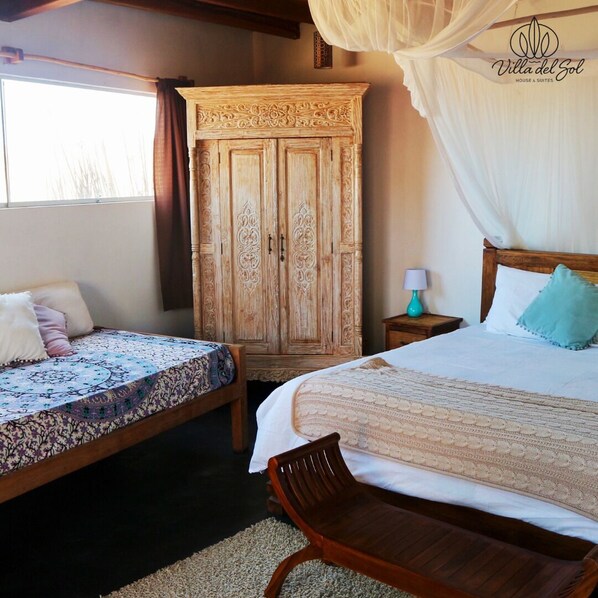 Une chambre avec deux lits, une armoire en bois, une chaise et une table de chevet avec une lampe.