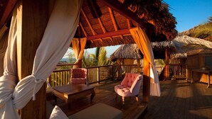 A wooden deck with a thatched roof structure, a cushioned bench, and two upholstered chairs. - Villa del Sol Mancora (Máncora)