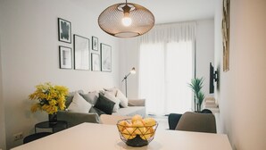 A modern living room with a dining table, a sofa, and a coffee table. There are framed pictures on the wall and a plant on the side.