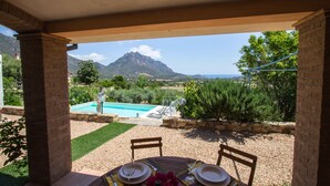A patio with a table set for dining, overlooking a swimming pool and a mountain view. - Villa Calu' - Wonderful villa in Sardinia with swimming pool and sea view (Tertenia)