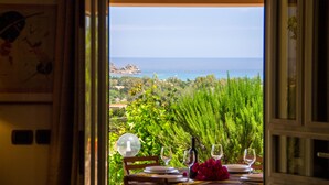 An open door leading to a dining area with a table set for two, a wine bottle, and a glass of wine. - Villa Calu' - Wonderful villa in Sardinia with swimming pool and sea view (Tertenia)
