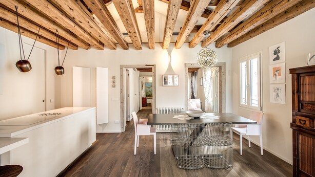 A modern kitchen with white cabinetry, a wooden ceiling, and a dining area with a metal table and chairs. - Exclusive apartment in the former Ospizio delle Donzelle, near Biennale Gardens (Venezia)