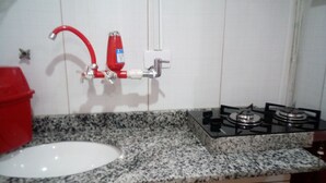 Een keuken met een granieten aanrecht, een witte wasbak, een rode kraan en een gasfornuis.