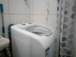 A compact, white, wall-mounted washing machine with a transparent door, located in a bathroom with tiled walls and a shower curtain with circular patterns. - Studio Vila Buarque, metro República and Sta Cecília 3 minutes away, pets accepted. (SP)