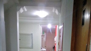 Een gang die leidt naar een kamer, met een deur aan de rechterkant, een raam met blinds aan de linkerkant en een betegelde vloer.