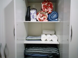 A wardrobe with shelves containing folded towels, a hairdryer, and a box. - Studio Vila Buarque, metro República and Sta Cecília 3 minutes away, pets accepted. (SP)