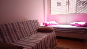 Een kamer met een gestreept bankje, een bed met roze beddengoed en een raam met een metalen hor.