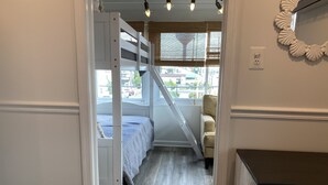 A bedroom with a bunk bed, a chair, a desk, and a window with blinds.