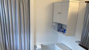 A bathroom with a shower curtain, toilet, cabinet, and sink.