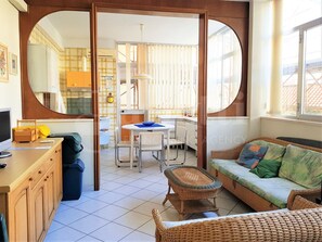 Un espacio habitable compacto con kitchenette, comedor y zona de estar con sofá y una pequeña mesa.