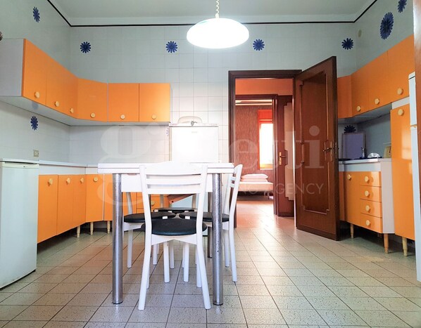 Una cocina compacta con armarios naranjas, una mesa blanca y dos sillas.