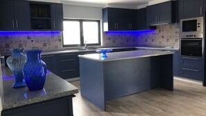 Une cuisine moderne avec des meubles de couleur sombre, un îlot central et un revêtement mural décoratif à motifs géométriques.