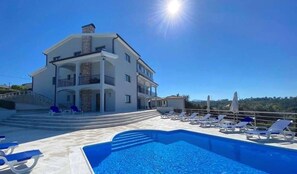 A two-story building with a swimming pool and sun loungers.
