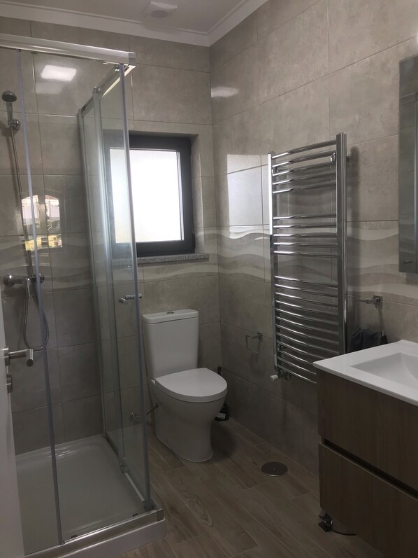 A modern bathroom with a glass-enclosed shower, a toilet, a sink, and a towel rack.