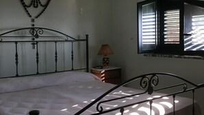 Une chambre à coucher comprenant un lit, une table de chevet, une lampe, un élément décoratif fixé au mur et une fenêtre avec des stores.