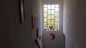 Un escalier étroit, avec une fenêtre en haut, une décoration en forme de croissant de lune rouge et une petite plante posée sur le rebord de la fenêtre.