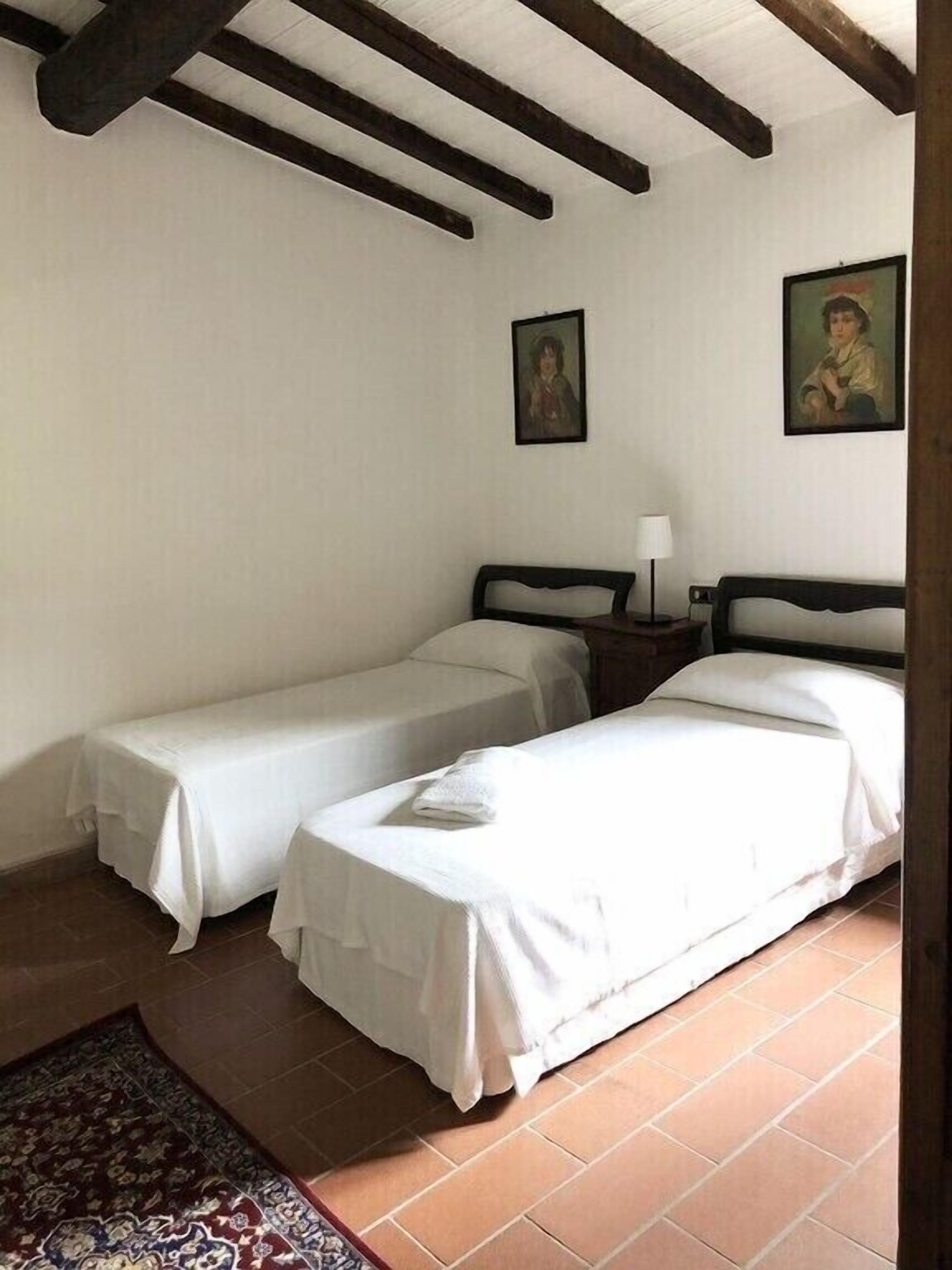 Een kamer met twee eenpersoonsbedden, een tafeltje met een lamp en twee ingelijste foto's aan de muur.