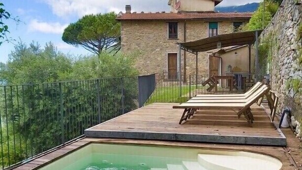 Una casa de piedra con piscina, terraza de madera y sillas de descanso.