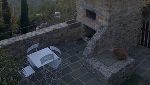 Un edificio de piedra con chimenea, una pequeña mesa con sillas y una planta en maceta.