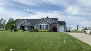 Une maison à deux étages avec un toit gris, un porche à l’avant et une pelouse bien entretenue.
