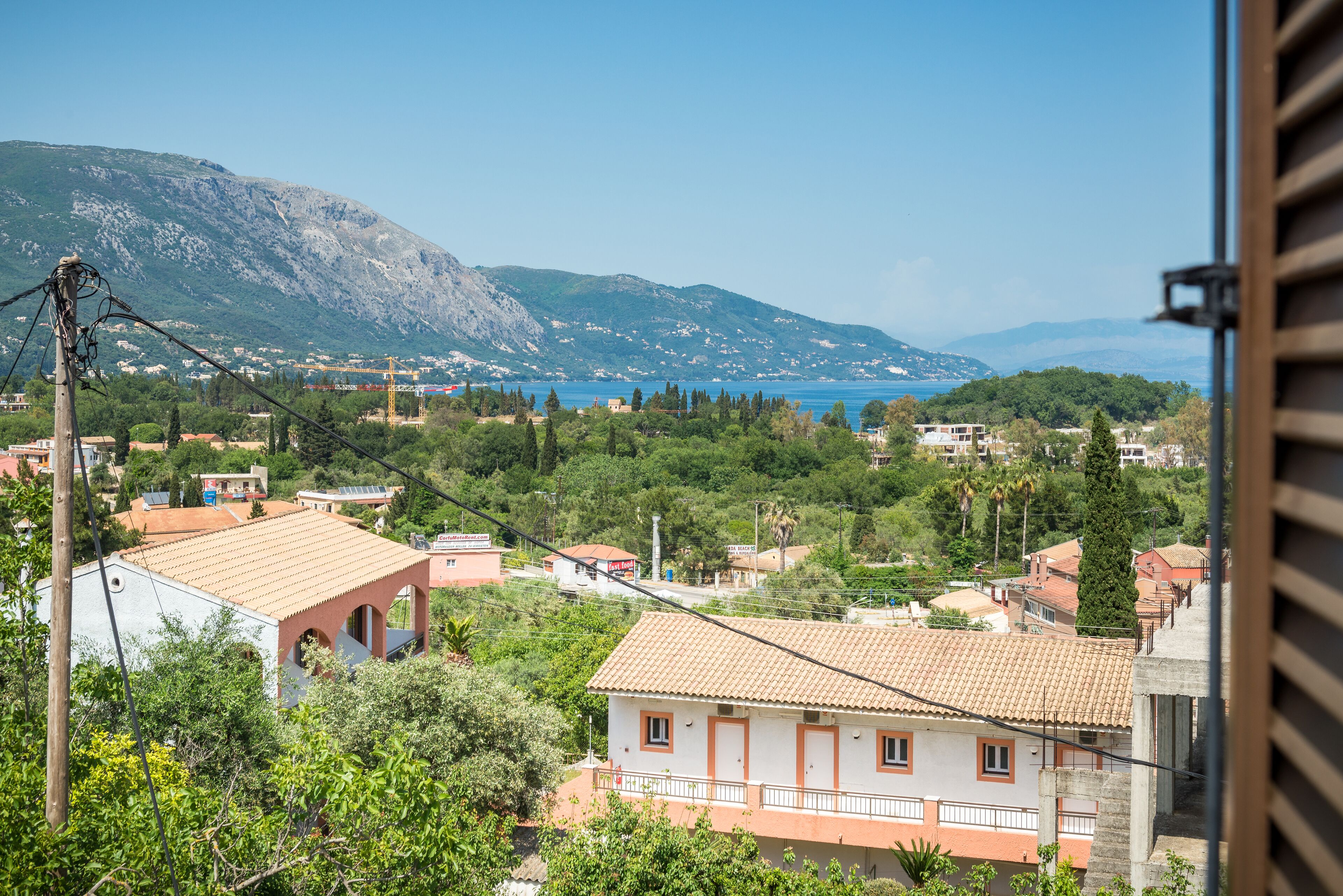 Uma vila costeira com edifícios de telhados em tons de terracota, uma montanha ao fundo e vista para o mar.