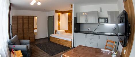 Una habitación compacta con una cama, un pequeño sofá, una mesa de madera y una kitchenette.
