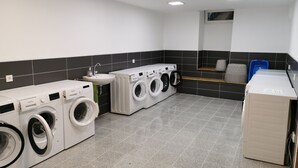 A laundry room with multiple washing machines, a sink, and a mirror. - LuPartment-Studio-Apartment-Stadtmitte (Ludwigshafen)