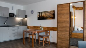 A compact living space with a kitchenette, a dining area with a table and chairs, a bed with a wooden headboard, and a painting of a bridge on the wall. - LuPartment-Studio-Apartment-Stadtmitte (Ludwigshafen)