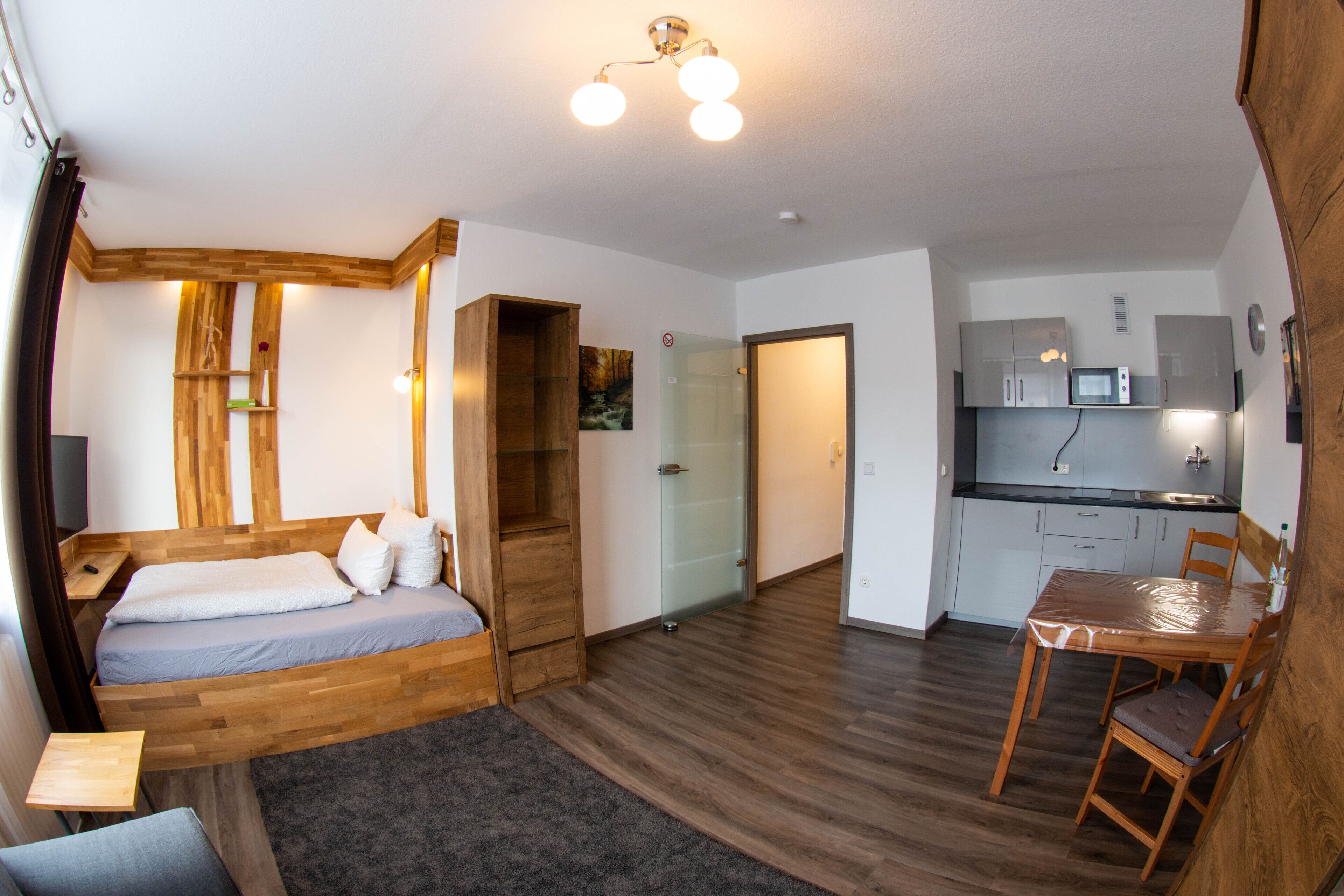 A compact room with a bed, a small table, and a kitchenette.