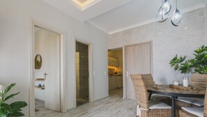 Een modern interieur met een eethoek, bestaande uit rieten stoelen en een houten tafel, een keuken met witte bakstenen muren en een gang die naar een andere kamer leidt.