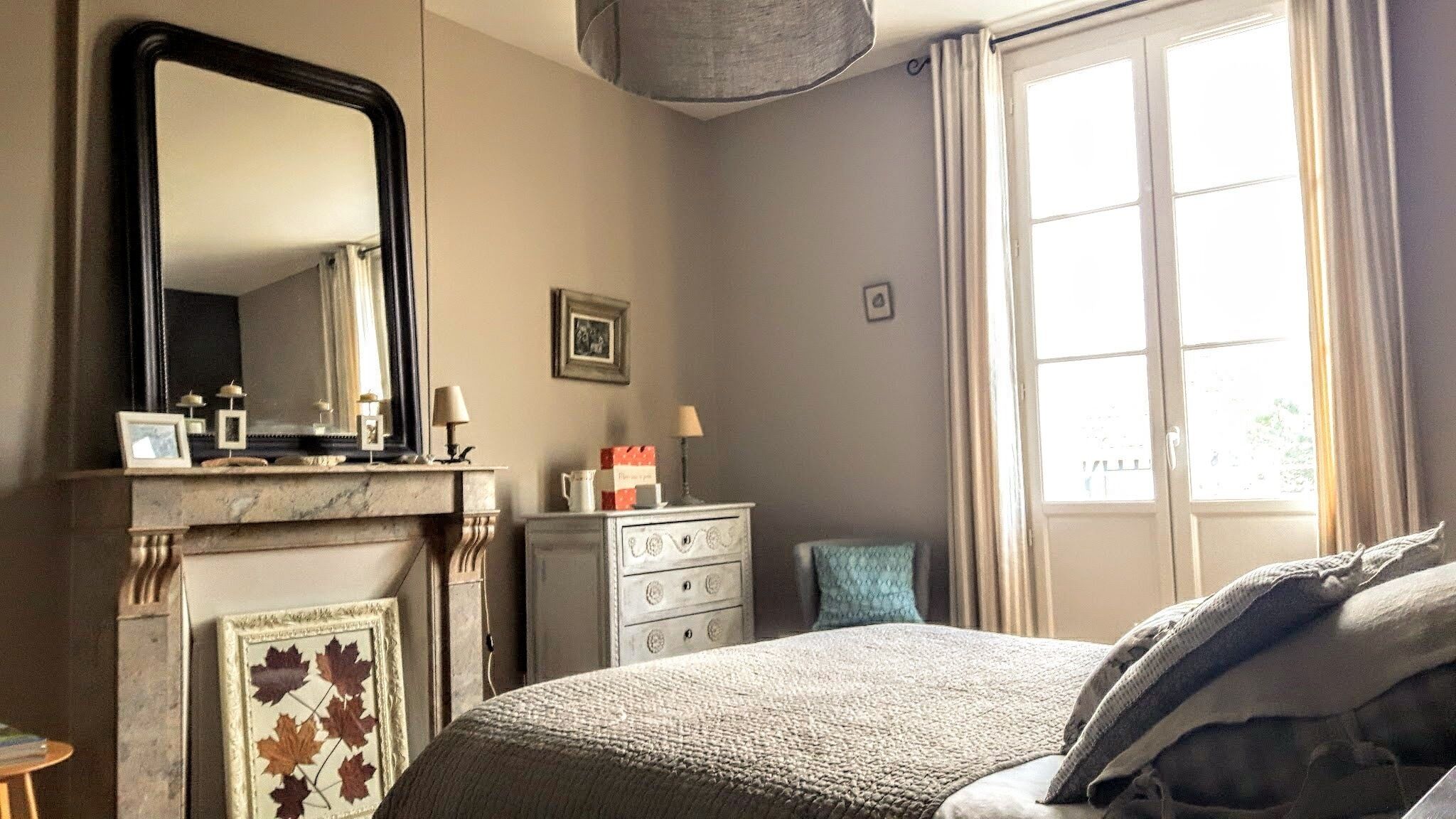 A bedroom with a bed, a dresser, a mirror, a fireplace, and a window.