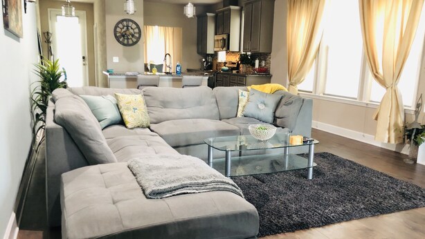 Een moderne woonkamer met een hoekbank, een glazen salontafel en een zwart vloerkleed.
