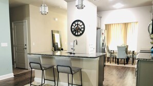 Een moderne keuken met een centraal eiland, een barkrukken, een klok en een eethoek met stoelen en een tafel.