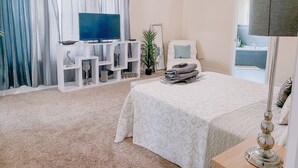 Een slaapkamer met een bed, televisie, nachtkastje, lamp en een badkamer die door een open deur zichtbaar is.