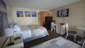 A hotel room with a bed, desk, chair, TV, and artwork on the wall. - Island Colony 715 Charming Studio with Pool View (Honolulu)
