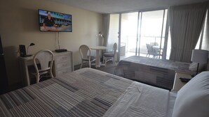 A hotel room with two beds, a desk, a chair, and a TV mounted on the wall. - Island Colony 715 Charming Studio with Pool View (Honolulu)