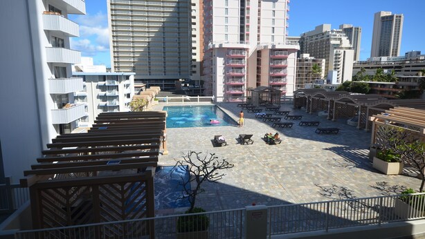 A rooftop pool area with lounge chairs, a swimming pool, and high-rise buildings in the background. - Island Colony 715 Charming Studio with Pool View (Honolulu)
