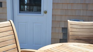 Une table et des chaises en bois se trouvent devant une maison avec une porte blanche et une fenêtre.