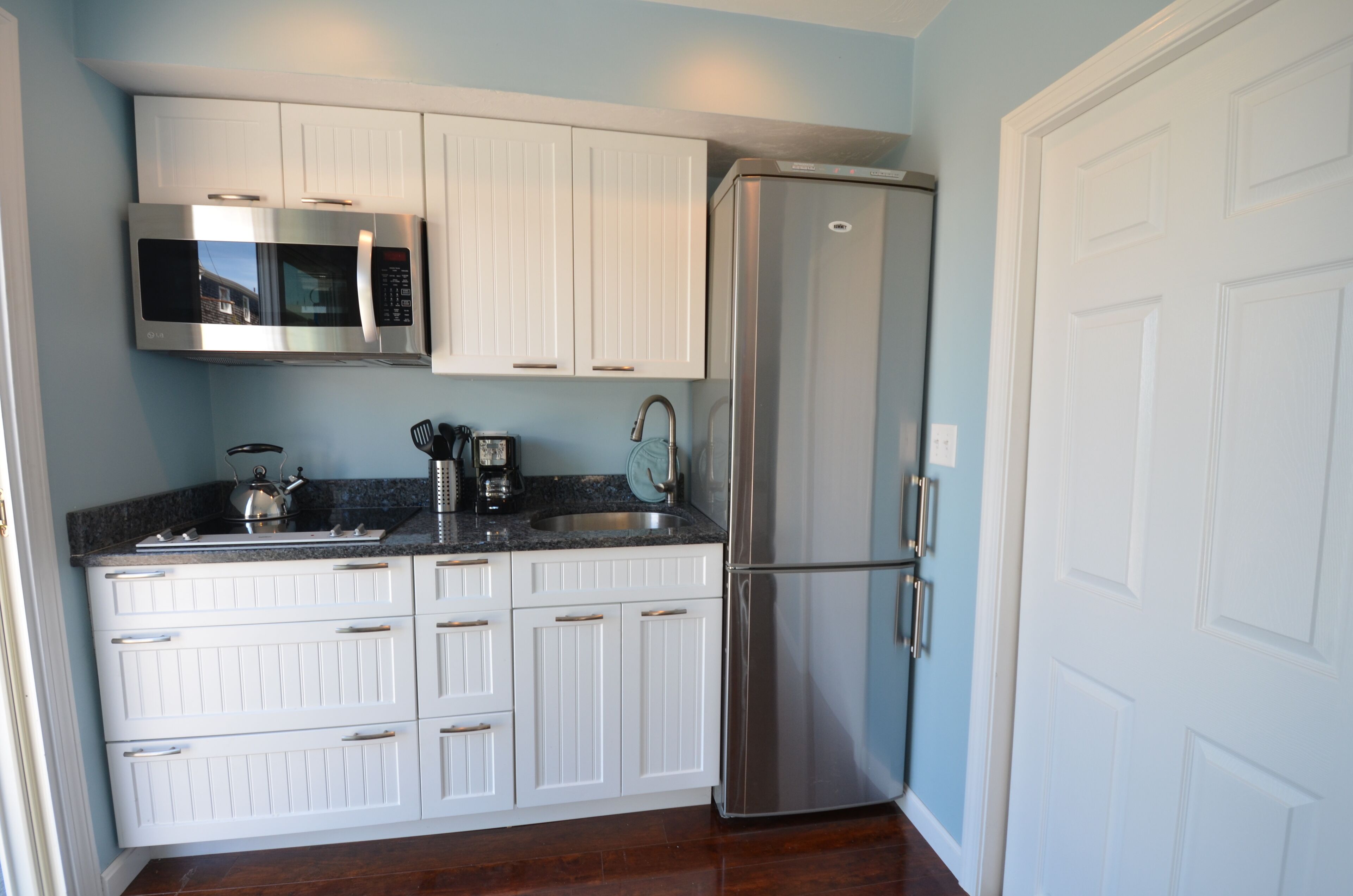 A kitchen with white cabinets, a stainless steel refrigerator, a microwave, and a sink.