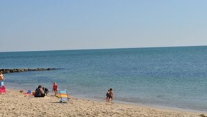 Une plage animée, une chaise de plage colorée à rayures et une eau calme.