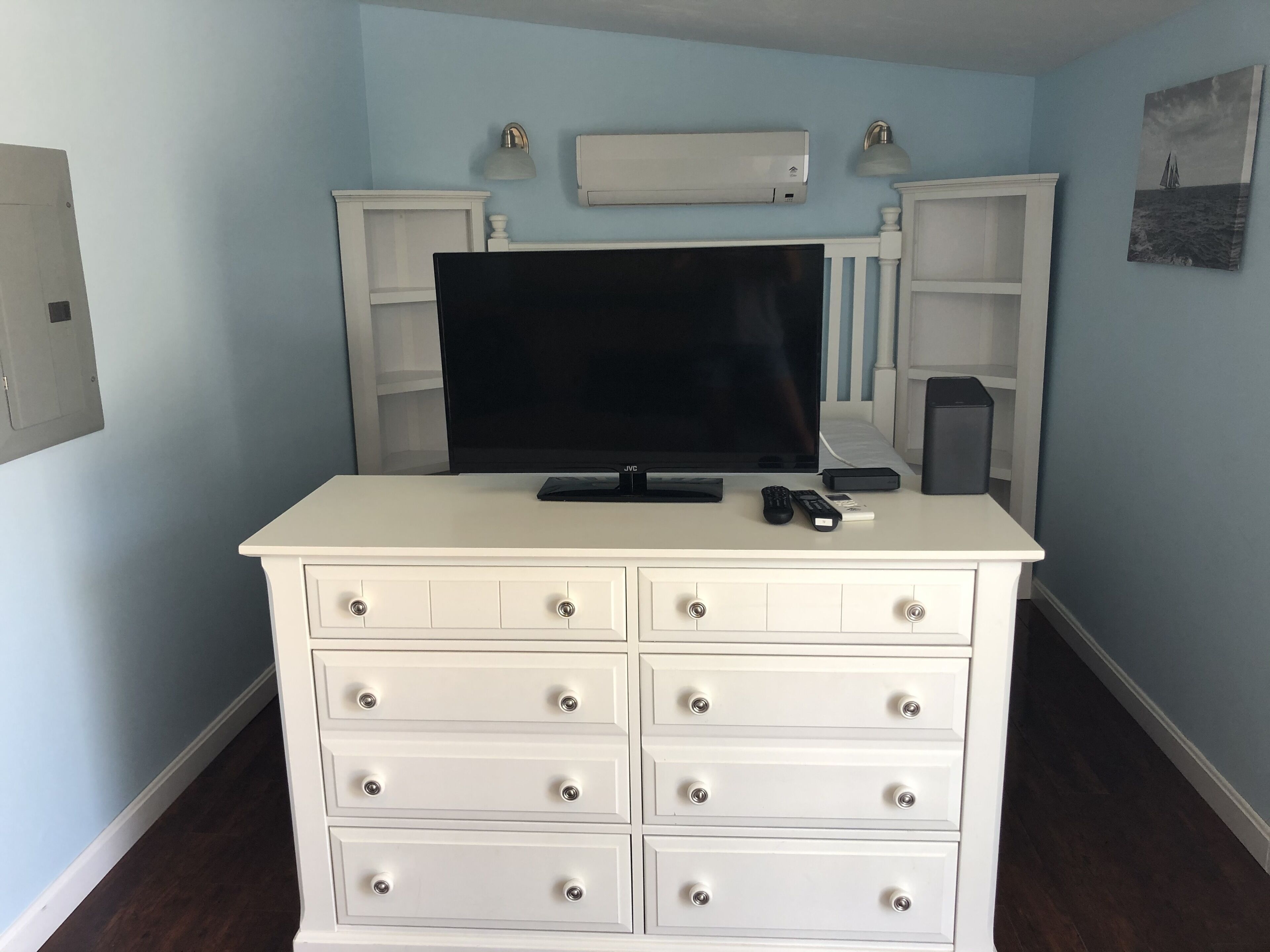 A white dresser with drawers and a flat-screen TV on top.