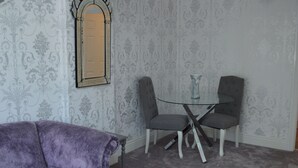 Ein Zimmer mit einem violetten Samsofa, einem kleinen Tisch, zwei Stühlen und einem Glastisch.
