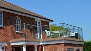 Ein zweigeschossiges Ziegelhaus mit einem Balkon, der mit Glasgeländern und Gartenmöbeln ausgestattet ist.