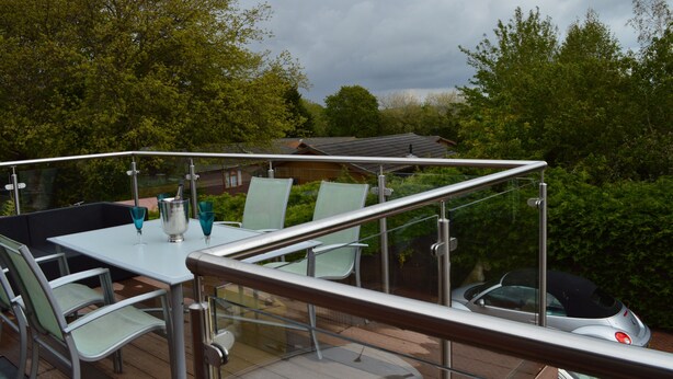 Eine Terrasse im Freien mit Glastrennwand, einem Tisch und Stühlen sowie Blick auf eine Wohngegend mit Bäumen und einem Haus.