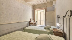 Een kleine, zwak verlichte kamer met twee bedden, een bureau en een stoel. Er is een raam met uitzicht.