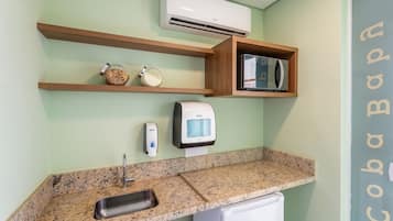 Uma cozinha com bancada de granito, pia, micro-ondas, máquina de café e uma pequena geladeira.