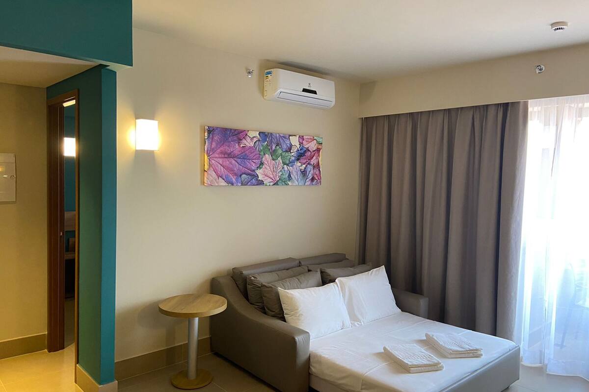 Hotelkamer met een bed, een bank, een klein tafeltje, een airconditioning, een schilderij en een raam met gordijnen.