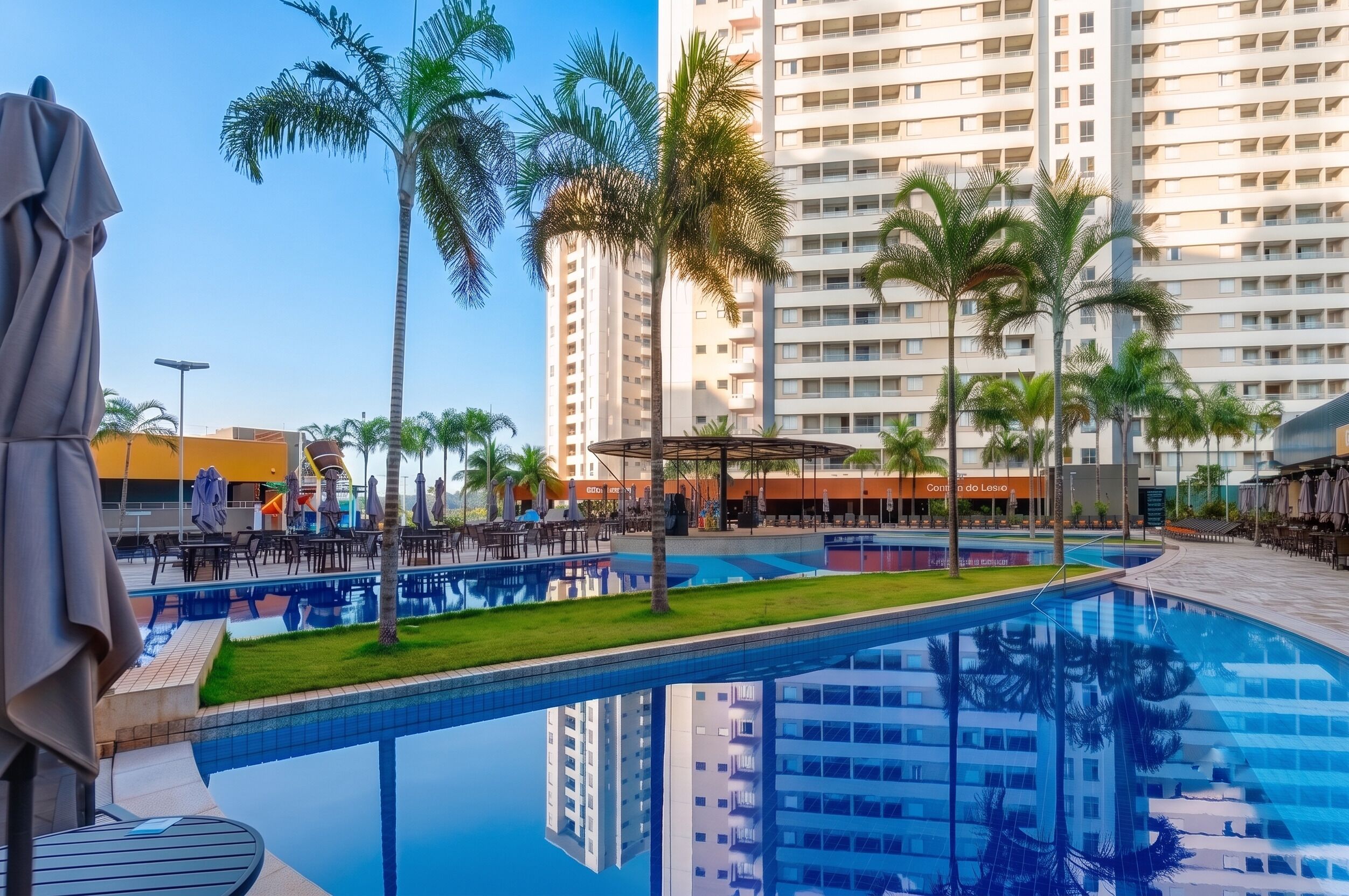Una piscina con palmeras, un área de descanso techada y un edificio alto al fondo.